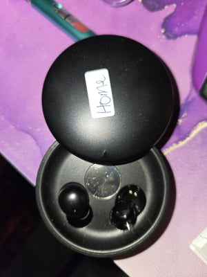 Open black charging case with both earbuds and a handwritten "Home" label
