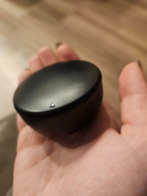 Closed round black charging case held in a palm