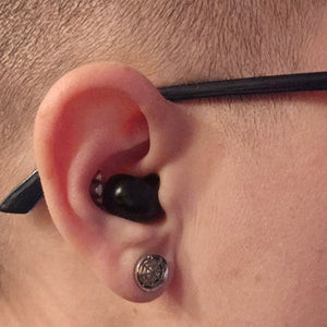 Close-up of an ear wearing the black earbud, glasses arm behind it, square crop