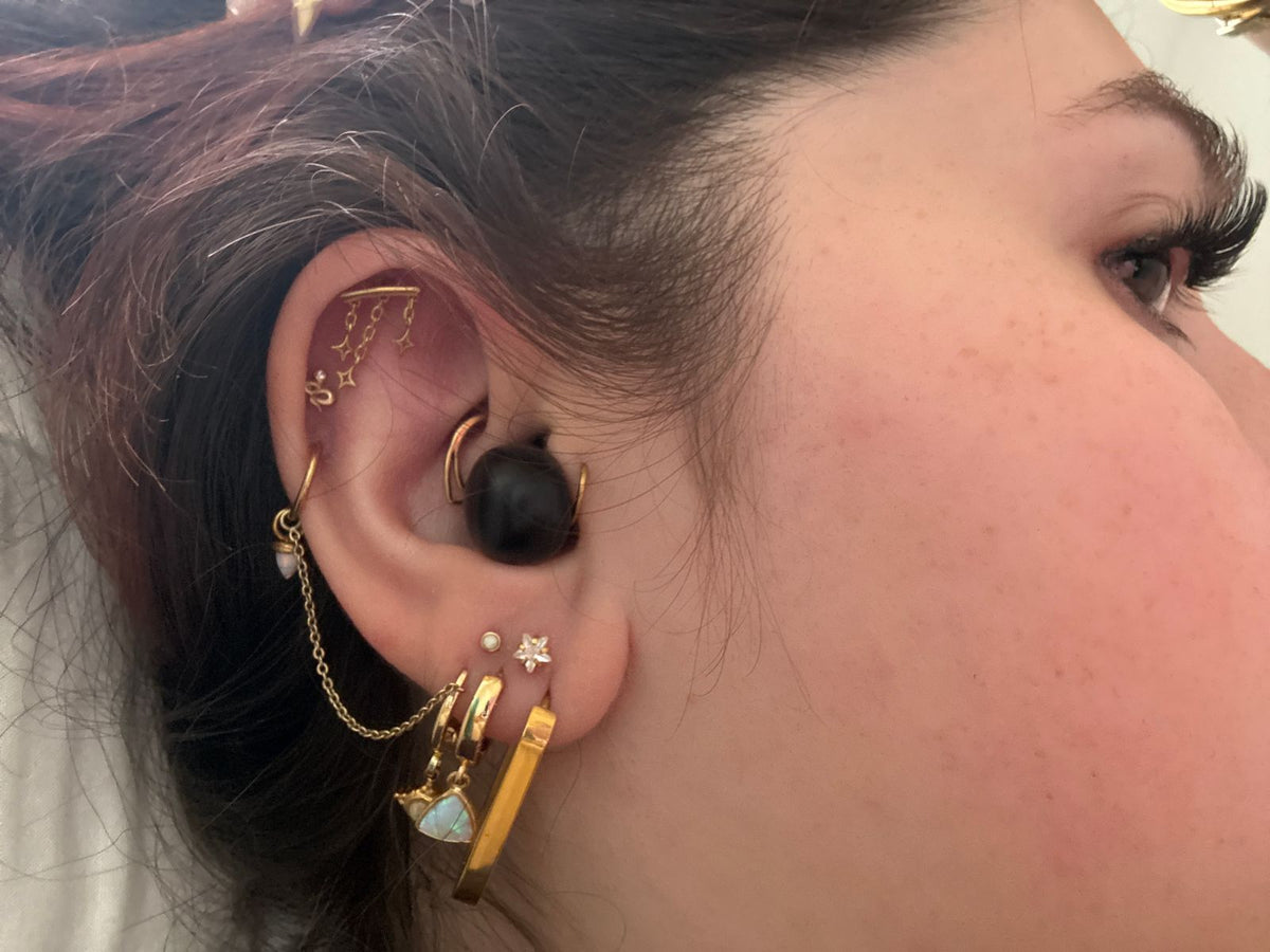Close-up of a woman with several ear piercings wearing the black earbud